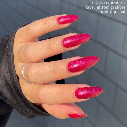 Closeup of nails painted in a lacquer that is bright red with an orange color shift and glitters.