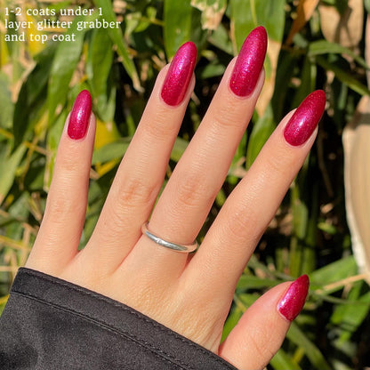 Closeup of nails painted in a lacquer that is bright red with an orange color shift and glitters.