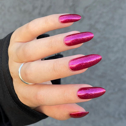 Closeup of nails painted in a lacquer that is bright red with an orange color shift and glitters.