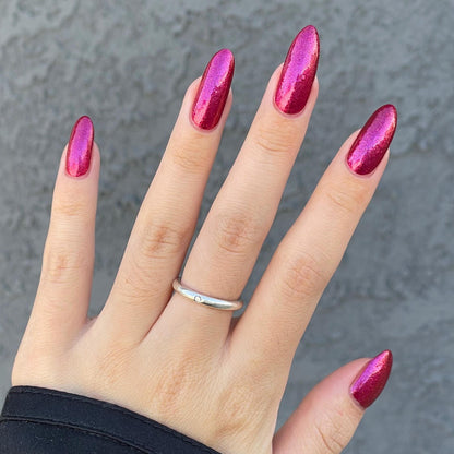 Closeup of nails painted in a lacquer that is bright red with an orange color shift and glitters.
