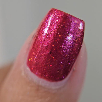 Closeup of a thumb painted in a lacquer that is bright red with an orange color shift and glitters.