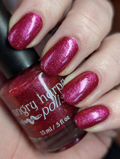Closeup of nails painted in a lacquer that is bright red with an orange color shift and glitters.