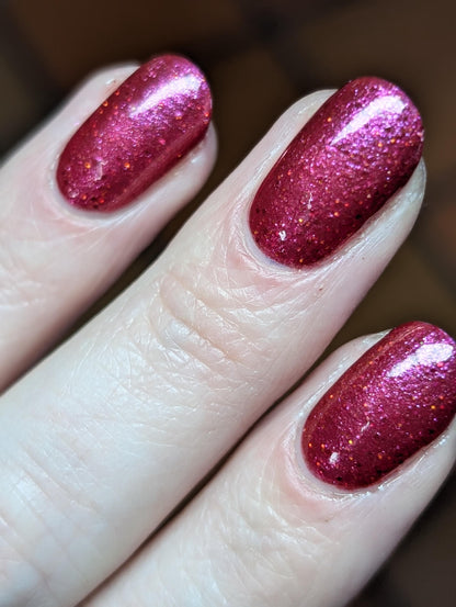 Closeup of nails painted in a lacquer that is bright red with an orange color shift and glitters.