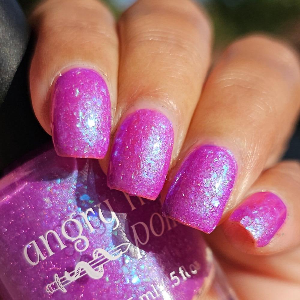 Closeup of nails painted in a lacquer that is bright pinkish purple sparkling with aqua shimmer and packed with iridescent flakes.