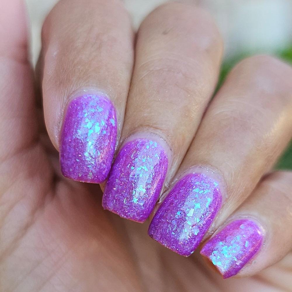 Closeup of nails painted in a lacquer that is bright pinkish purple sparkling with aqua shimmer and packed with iridescent flakes.