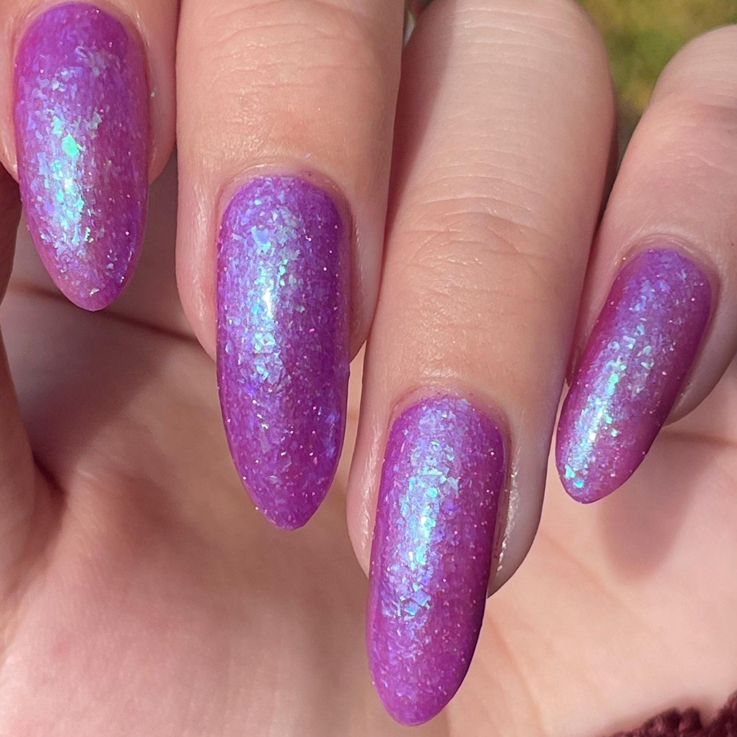 Closeup of nails painted in a lacquer that is bright pinkish purple sparkling with aqua shimmer and packed with iridescent flakes.