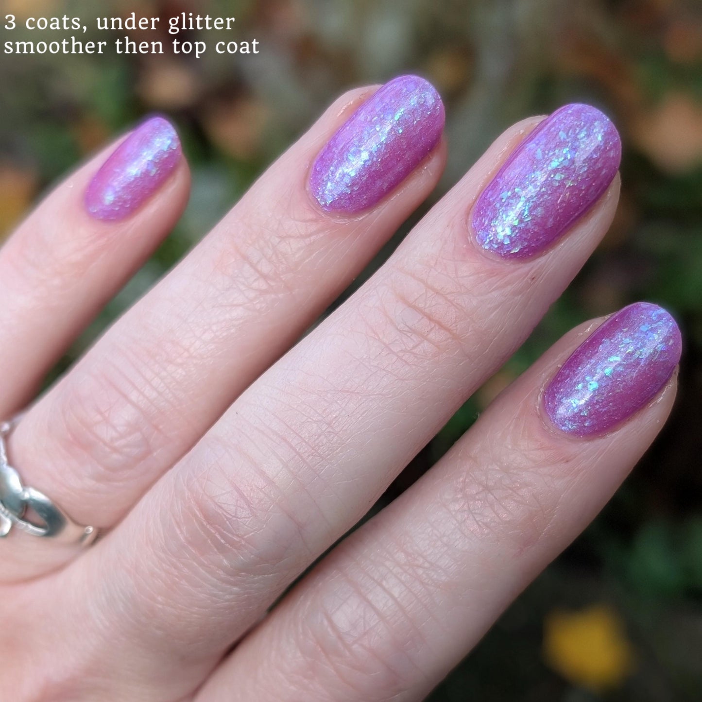 Closeup of nails painted in a lacquer that is bright pinkish purple sparkling with aqua shimmer and packed with iridescent flakes.