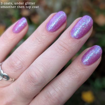 Closeup of nails painted in a lacquer that is bright pinkish purple sparkling with aqua shimmer and packed with iridescent flakes.