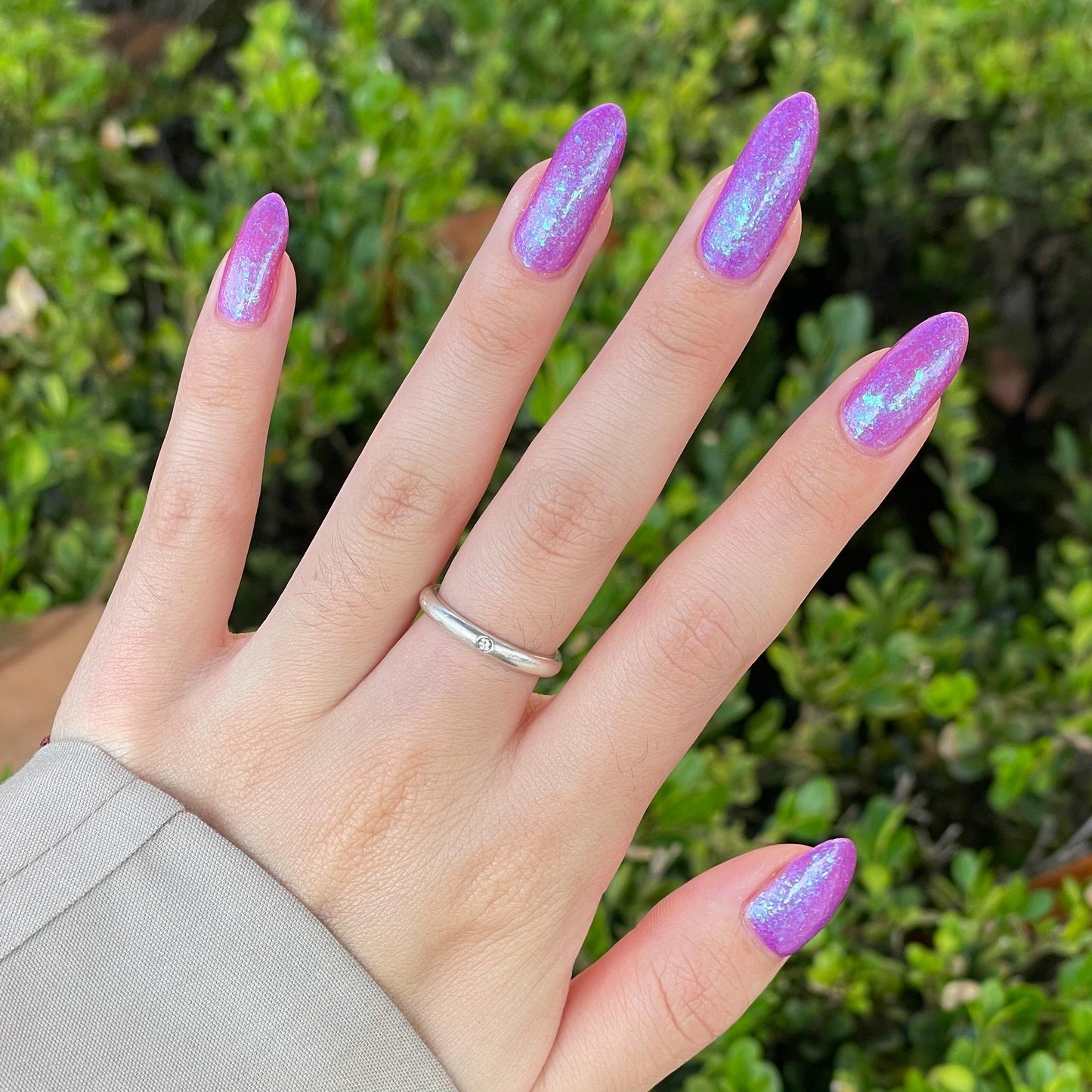Closeup of nails painted in a lacquer that is bright pinkish purple sparkling with aqua shimmer and packed with iridescent flakes.