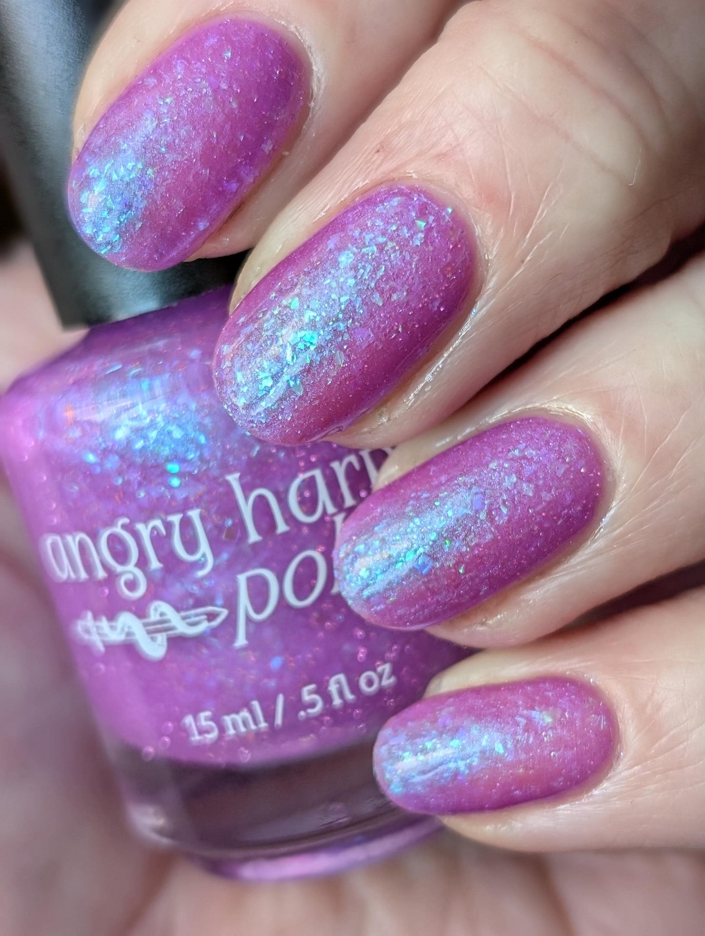 Closeup of nails painted in a lacquer that is bright pinkish purple sparkling with aqua shimmer and packed with iridescent flakes.