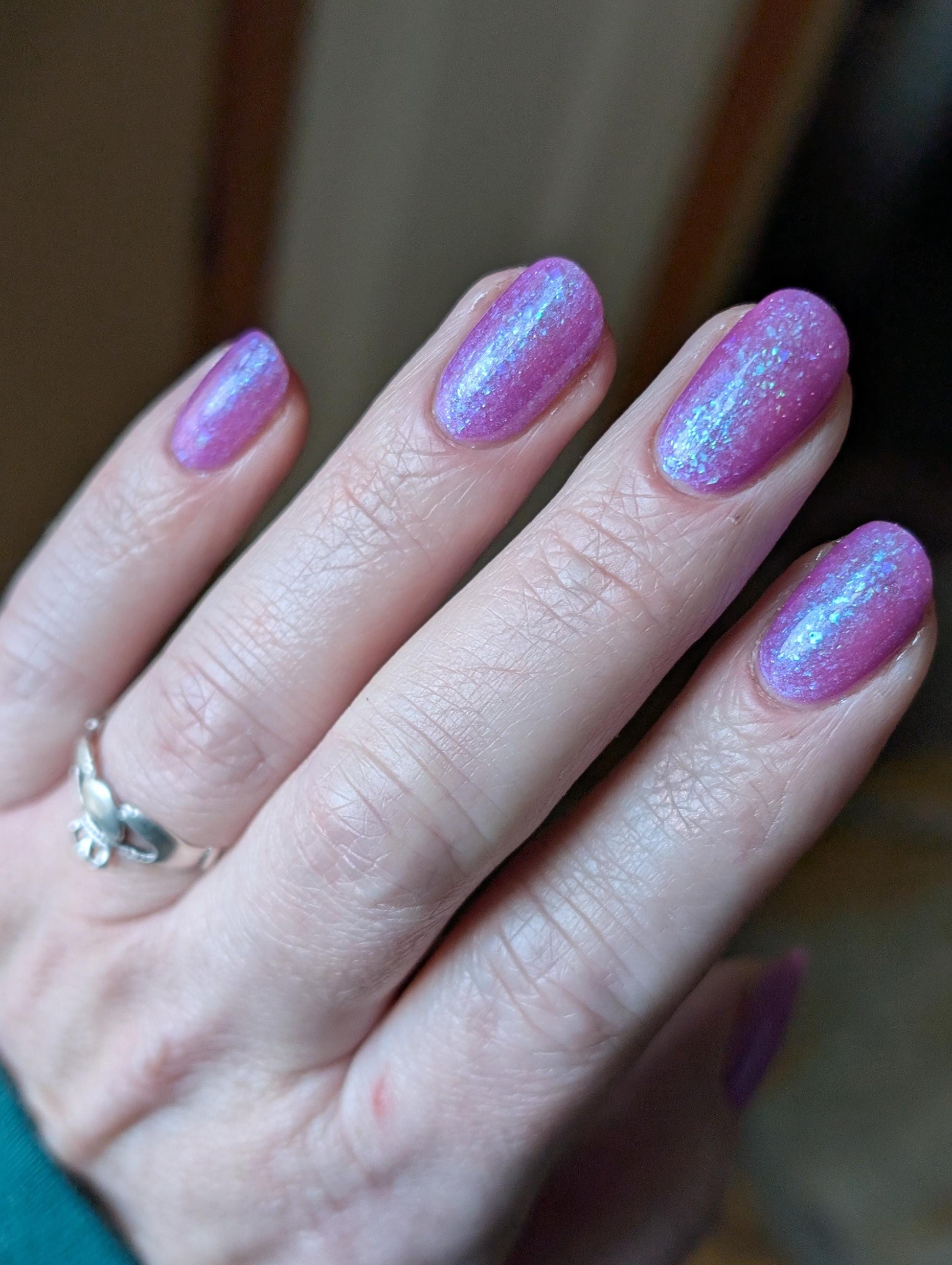 Closeup of nails painted in a lacquer that is bright pinkish purple sparkling with aqua shimmer and packed with iridescent flakes.