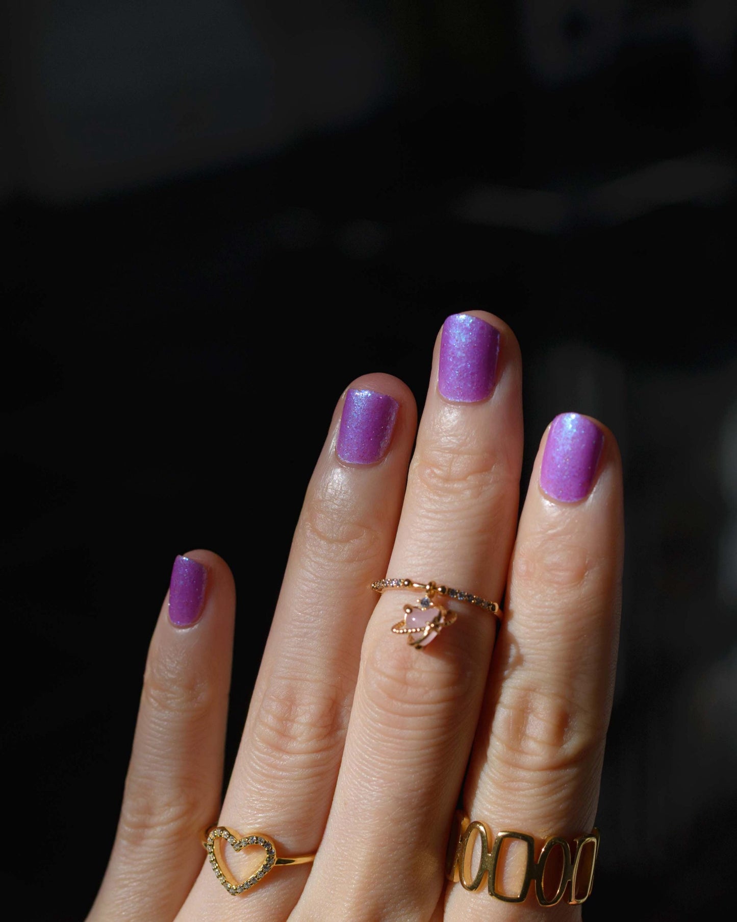 Closeup of nails painted in a lacquer that is bright pinkish purple sparkling with aqua shimmer and packed with iridescent flakes.