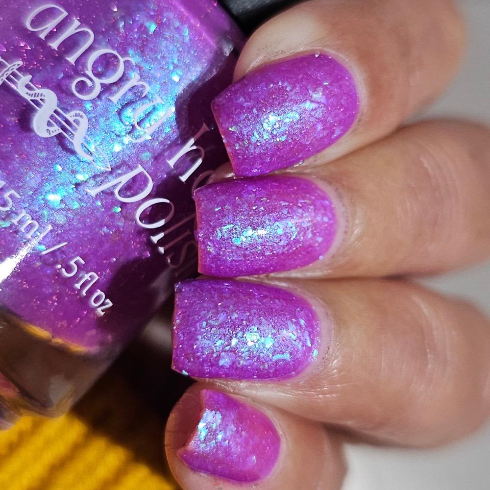 Closeup of nails painted in a lacquer that is bright pinkish purple sparkling with aqua shimmer and packed with iridescent flakes.