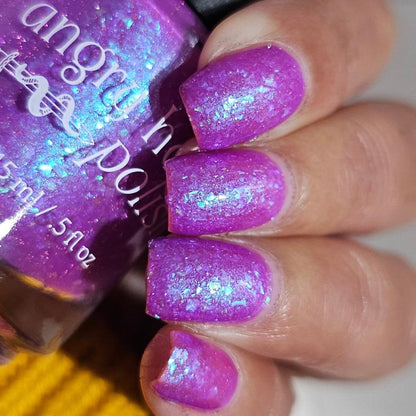 Closeup of nails painted in a lacquer that is bright pinkish purple sparkling with aqua shimmer and packed with iridescent flakes.