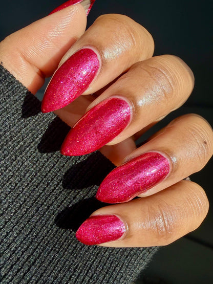 Closeup of nails painted in a lacquer that is bright red with an orange color shift and glitters.
