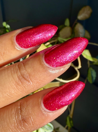 Closeup of nails painted in a lacquer that is bright red with an orange color shift and glitters.