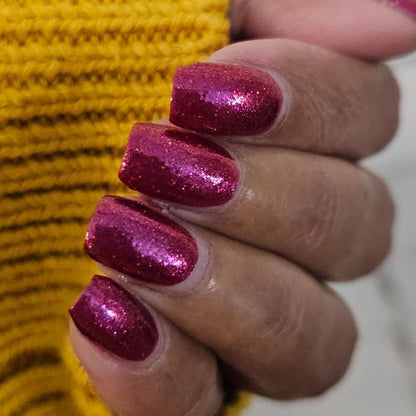 Closeup of nails painted in a lacquer that is bright red with an orange color shift and glitters.