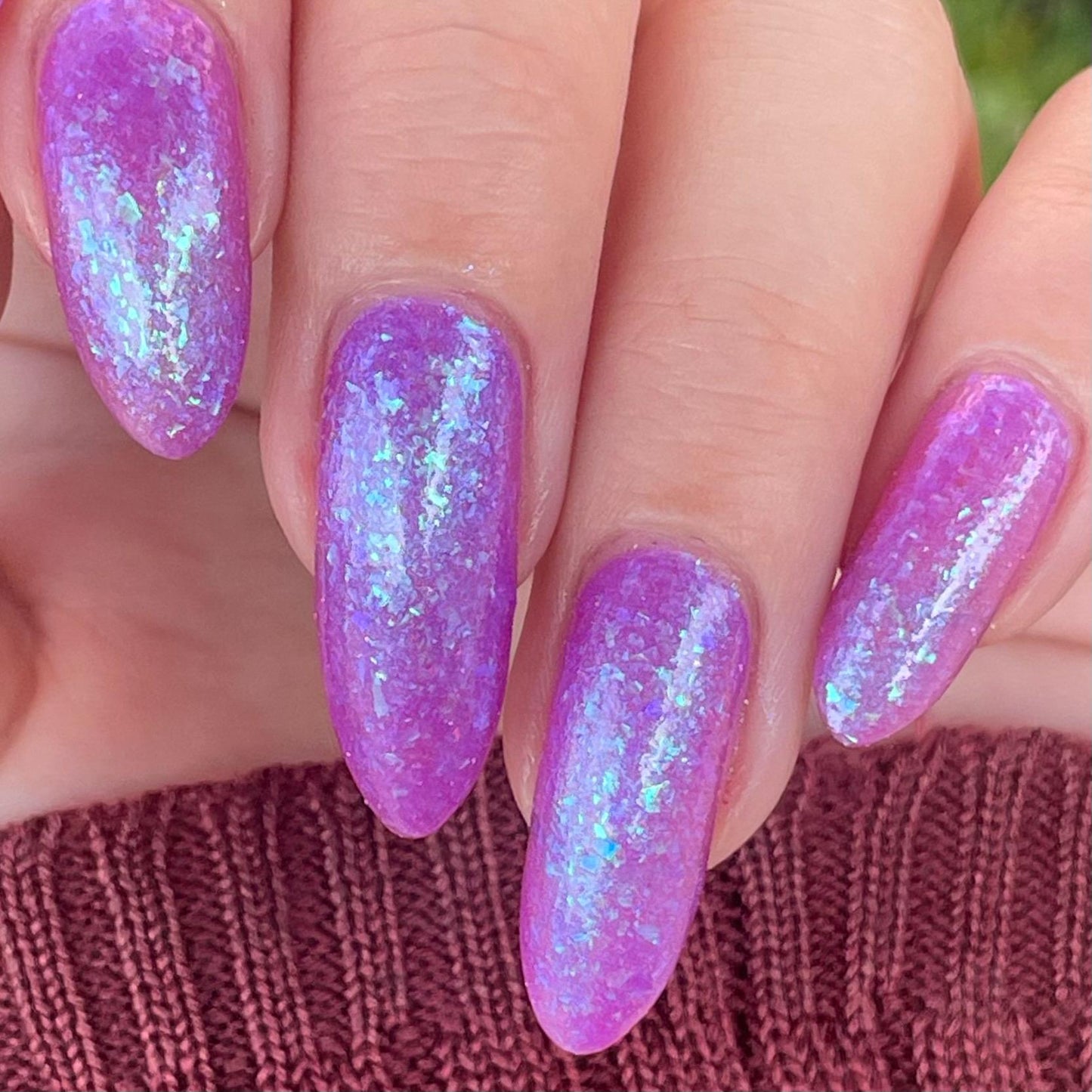 Closeup of nails painted in a lacquer that is bright pinkish purple sparkling with aqua shimmer and packed with iridescent flakes.