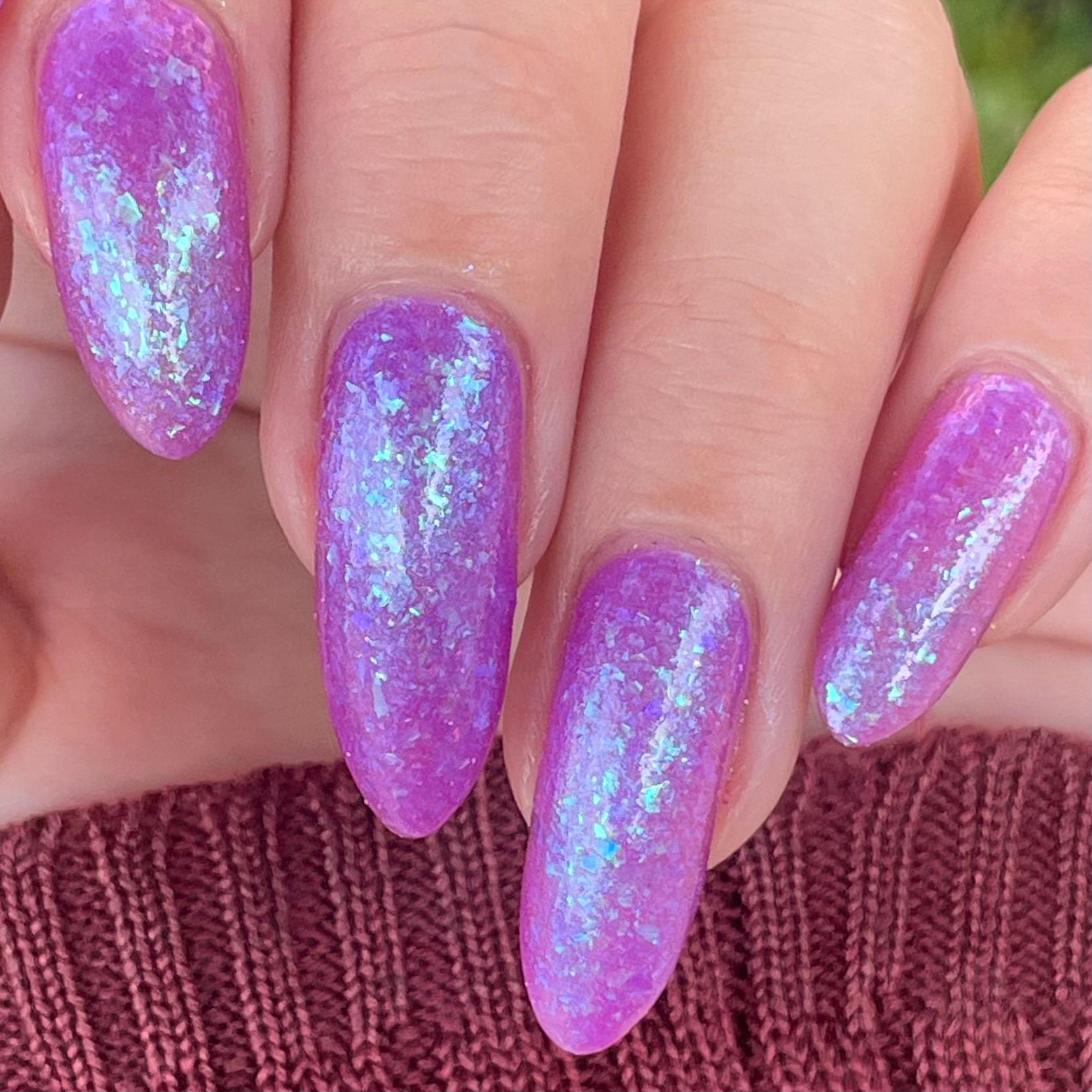 Closeup of nails painted in a lacquer that is bright pinkish purple sparkling with aqua shimmer and packed with iridescent flakes.