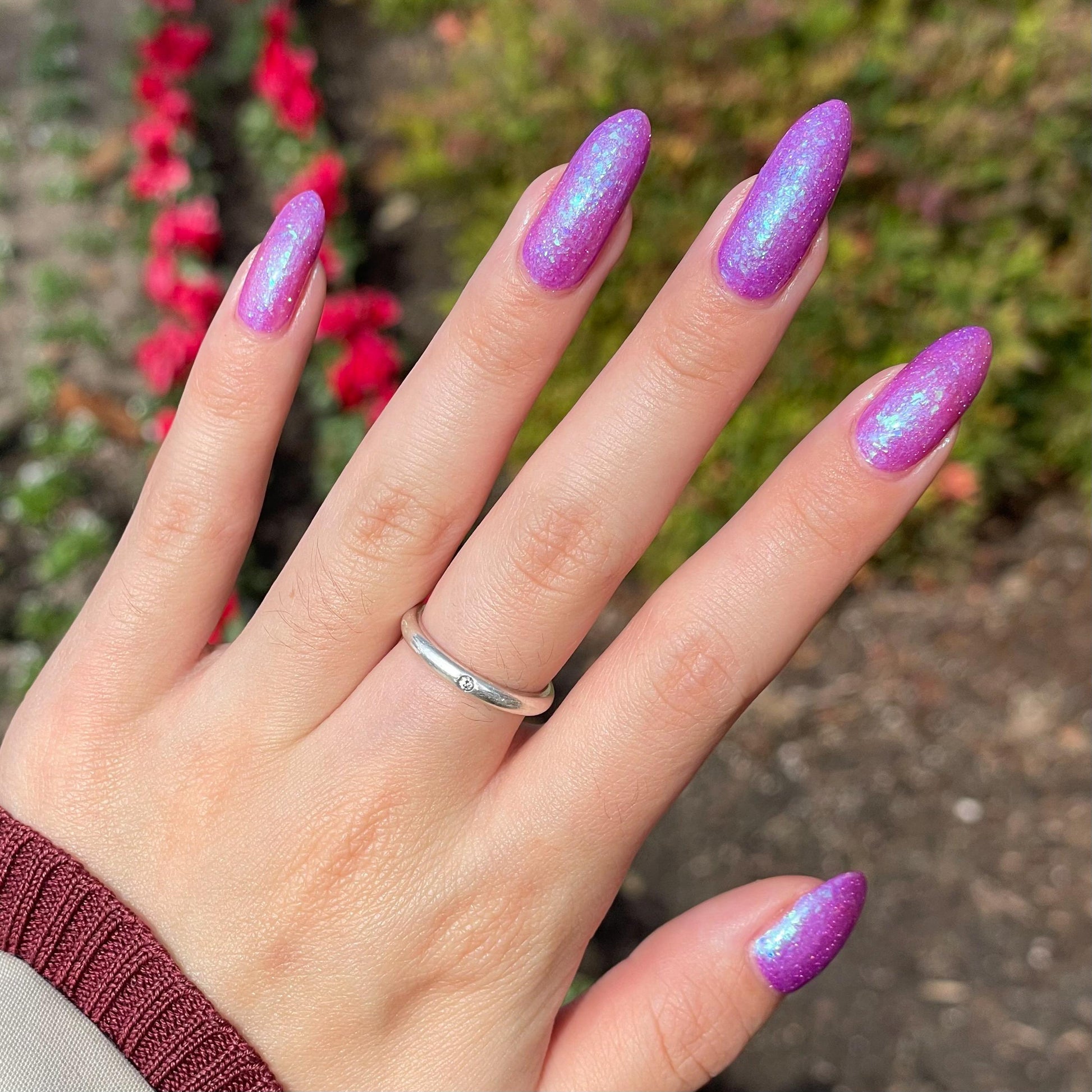 Closeup of nails painted in a lacquer that is bright pinkish purple sparkling with aqua shimmer and packed with iridescent flakes.
