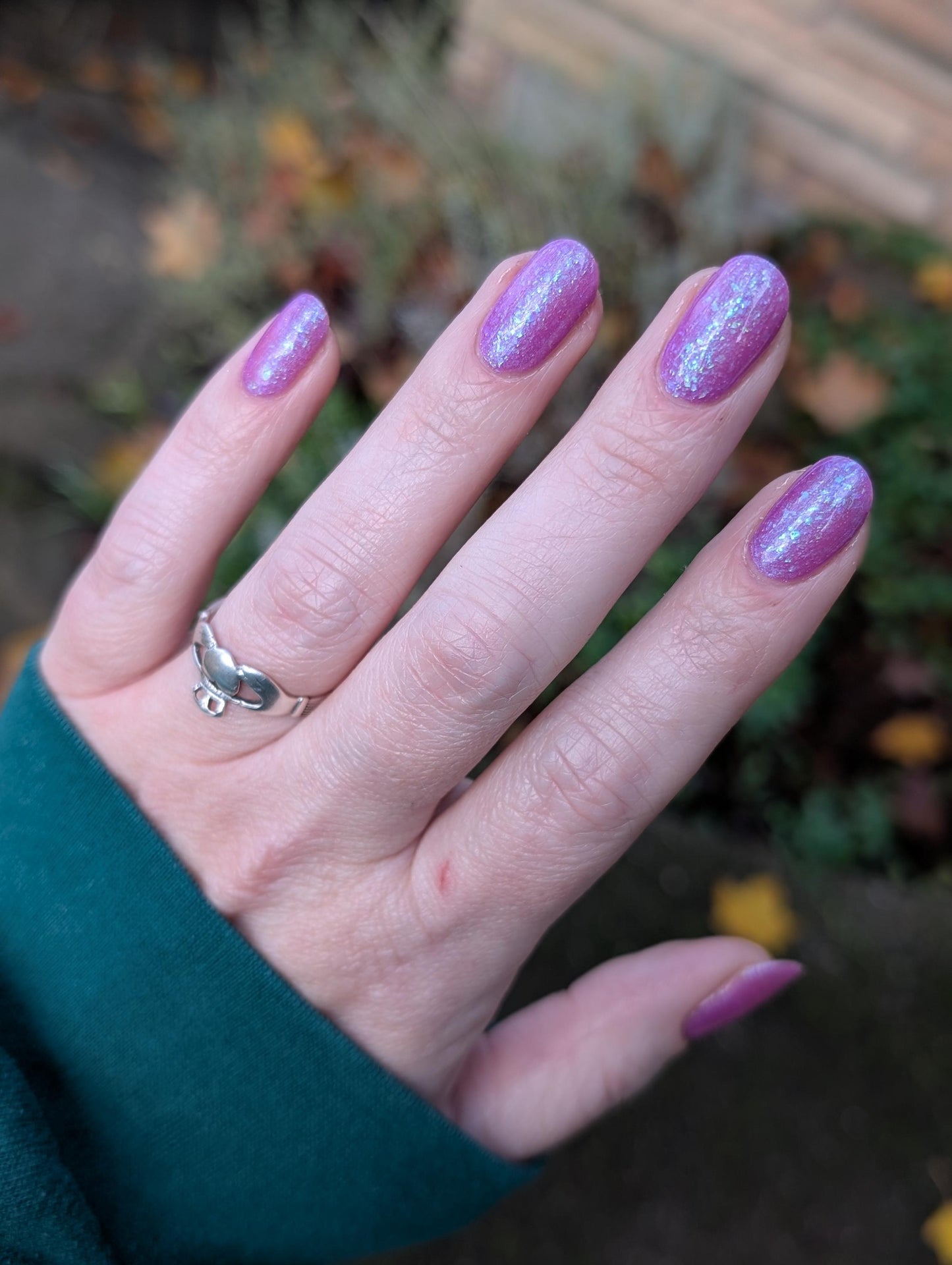 Closeup of nails painted in a lacquer that is bright pinkish purple sparkling with aqua shimmer and packed with iridescent flakes.
