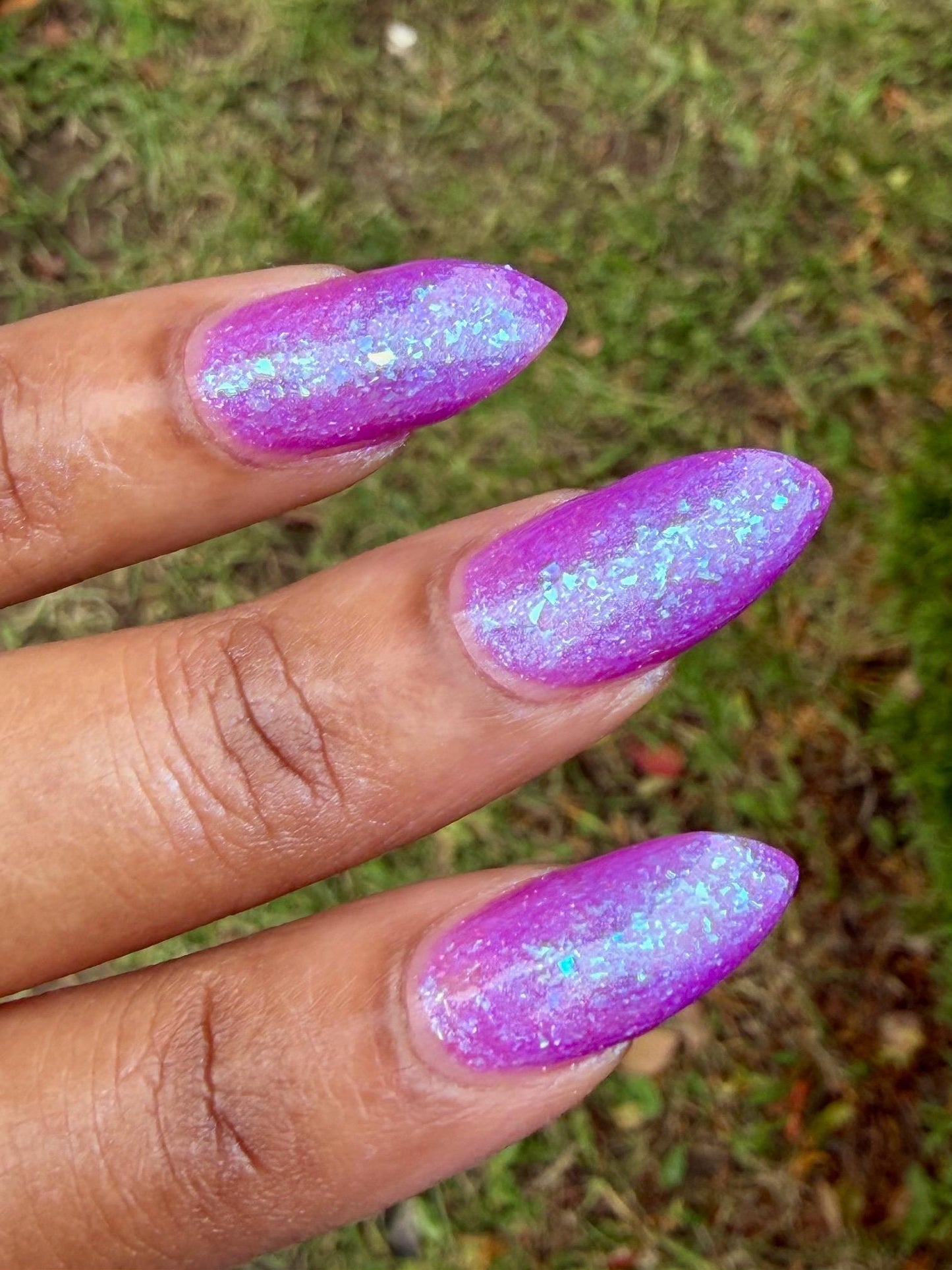 Closeup of nails painted in a lacquer that is bright pinkish purple sparkling with aqua shimmer and packed with iridescent flakes.