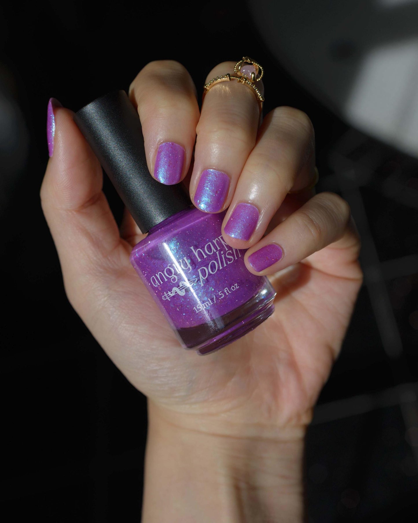 Closeup of nails painted in a lacquer that is bright pinkish purple sparkling with aqua shimmer and packed with iridescent flakes.