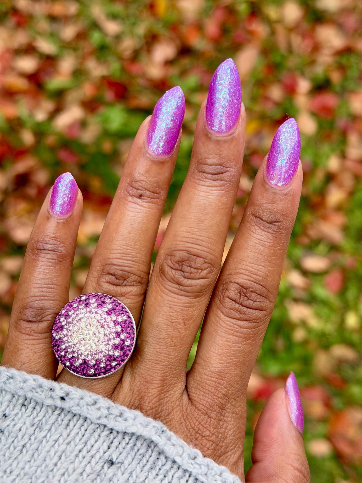 Closeup of nails painted in a lacquer that is bright pinkish purple sparkling with aqua shimmer and packed with iridescent flakes.