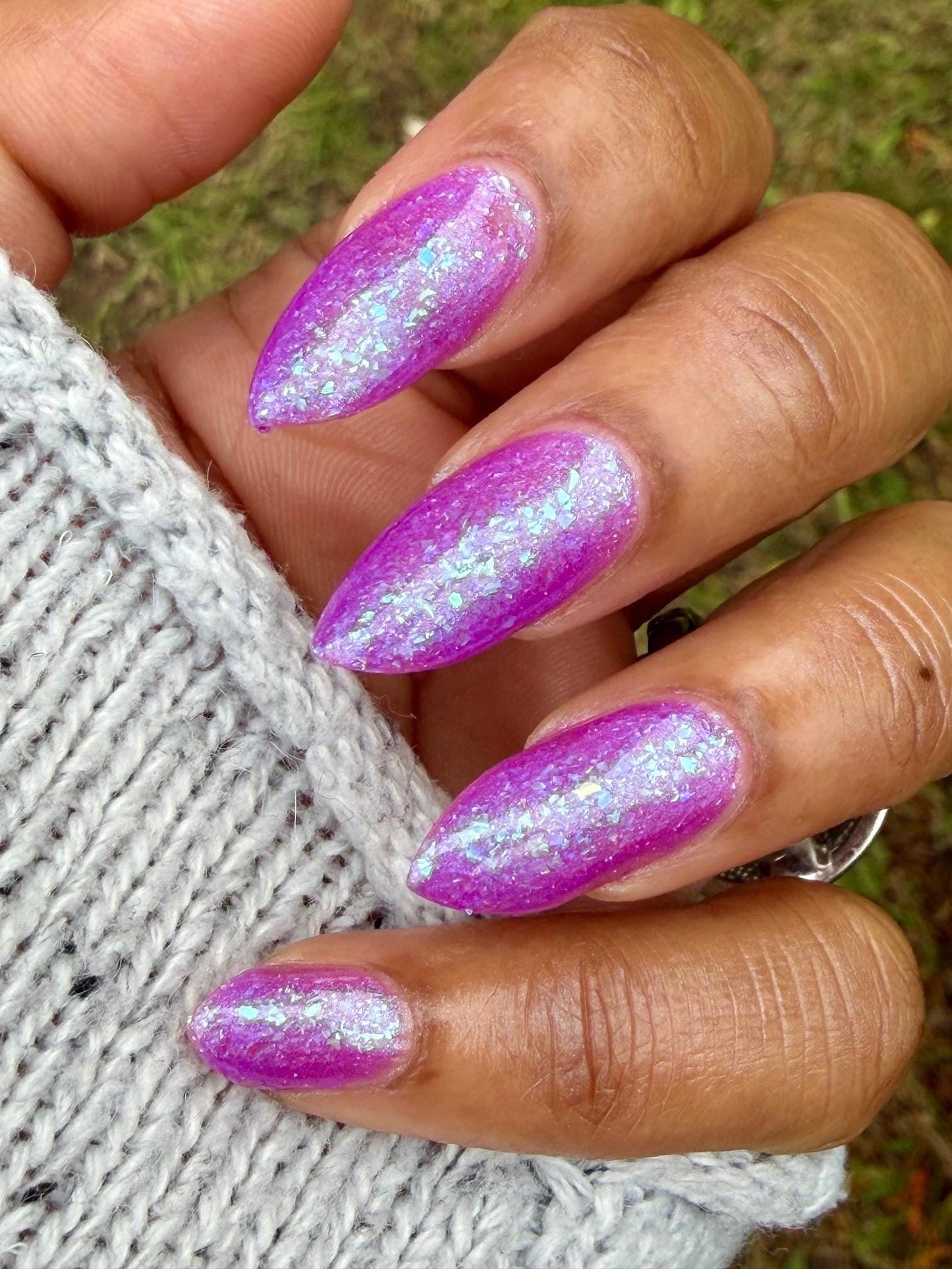 Closeup of nails painted in a lacquer that is bright pinkish purple sparkling with aqua shimmer and packed with iridescent flakes.