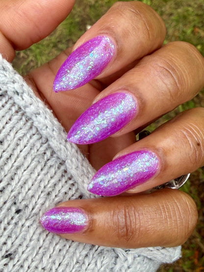 Closeup of nails painted in a lacquer that is bright pinkish purple sparkling with aqua shimmer and packed with iridescent flakes.