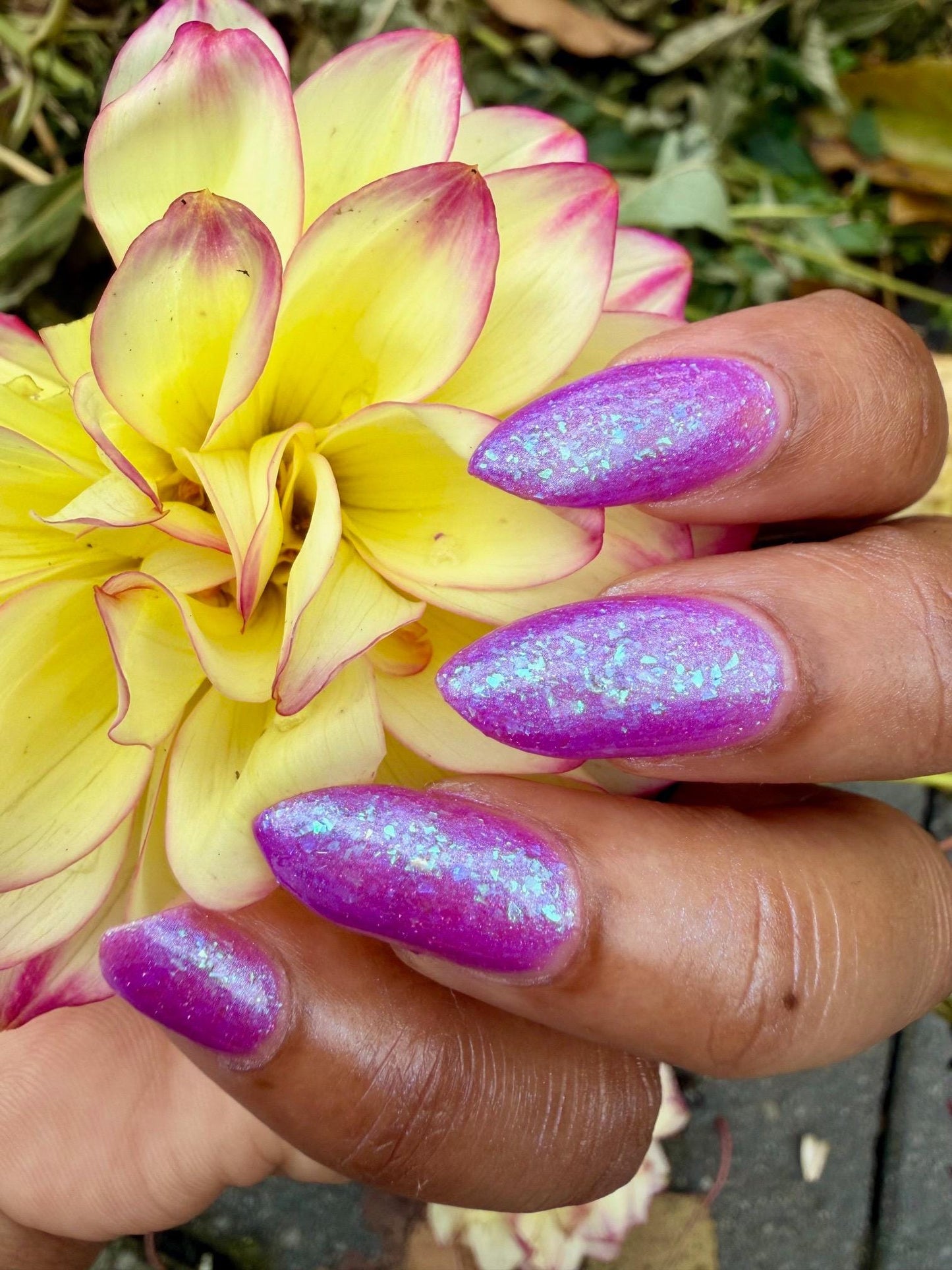 Closeup of nails painted in a lacquer that is bright pinkish purple sparkling with aqua shimmer and packed with iridescent flakes.