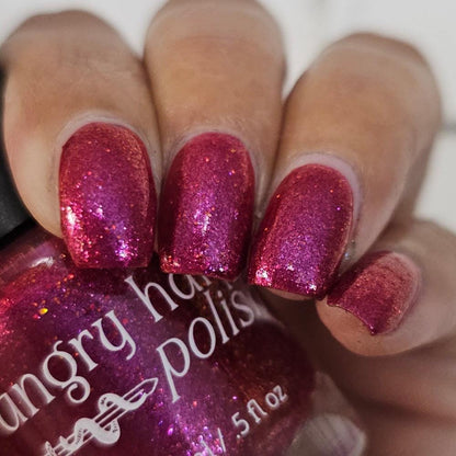 Closeup of nails painted in a lacquer that is bright red with an orange color shift and glitters.