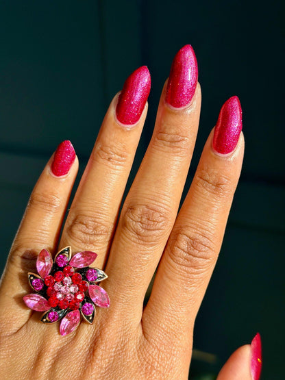 Closeup of nails painted in a lacquer that is bright red with an orange color shift and glitters.