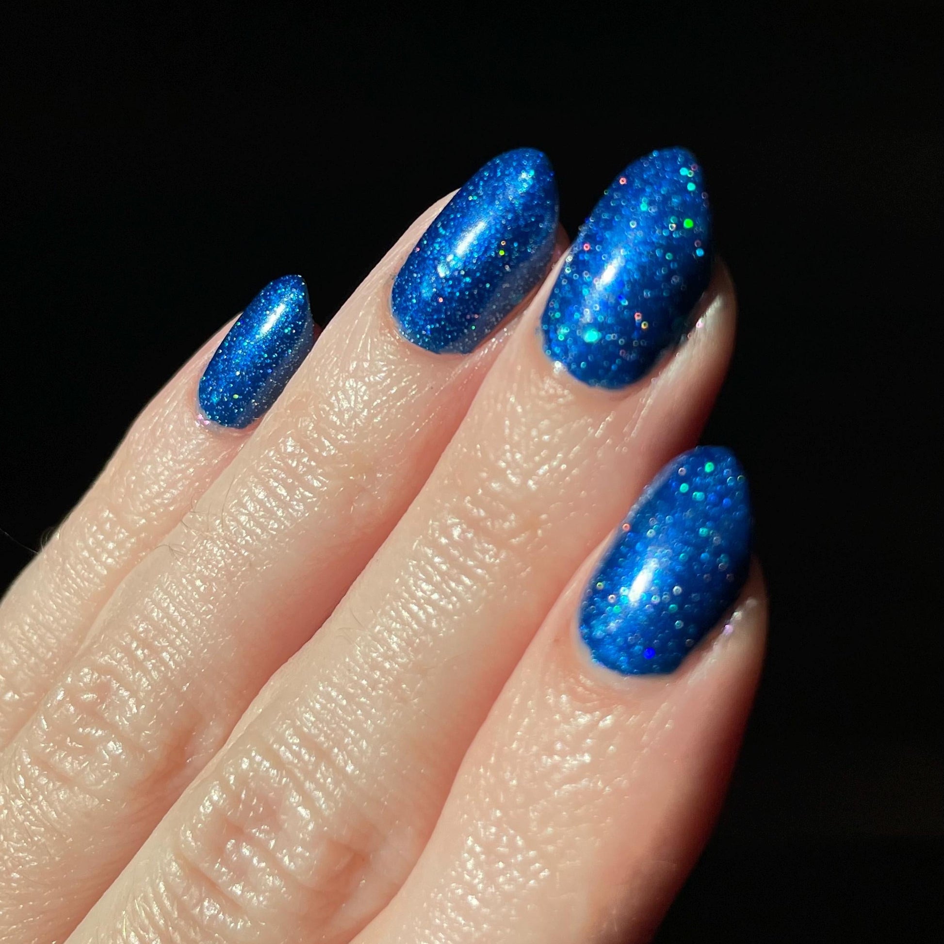 Finger with blue glittery nail polish on a black background