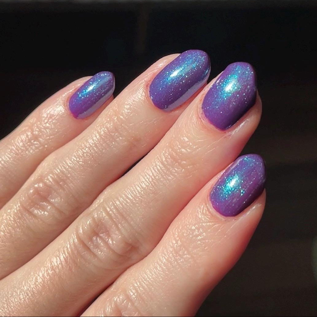 Hand with purple glittery nail polish on a dark background