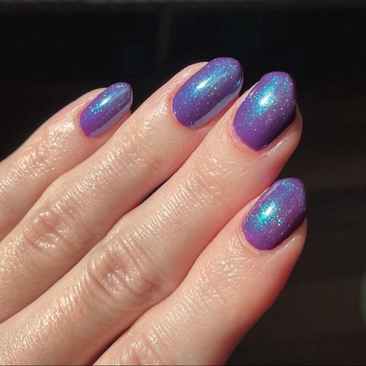 Hand with purple glittery nail polish on a dark background