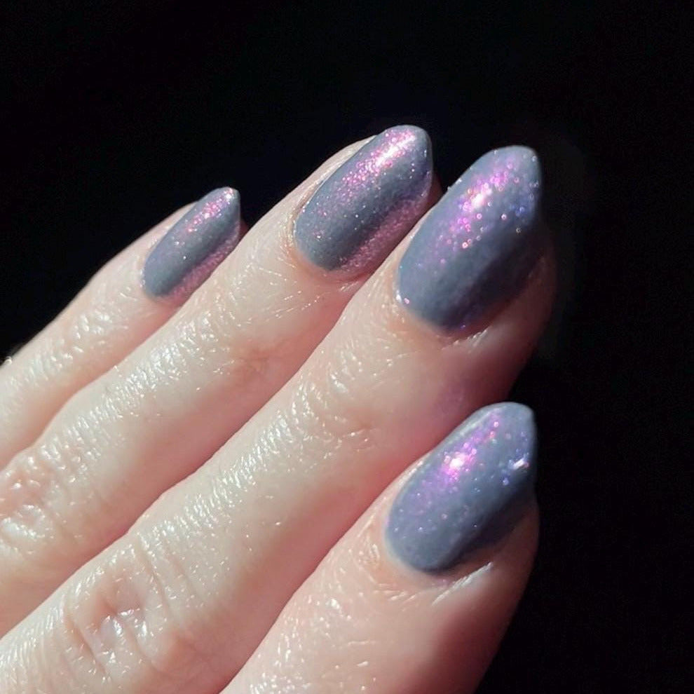 Close-up of a hand with light purple glittery nail polish on a dark background