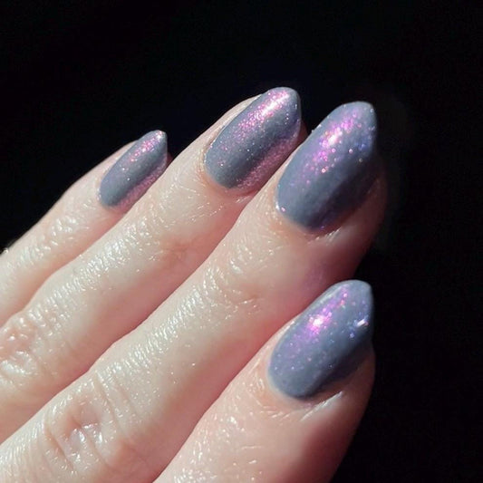 Close-up of a hand with light purple glittery nail polish on a dark background