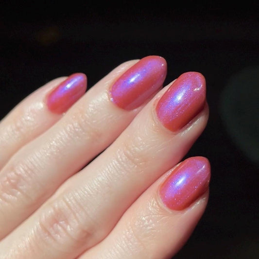 Hand with orange shimmery nail polish on a dark background