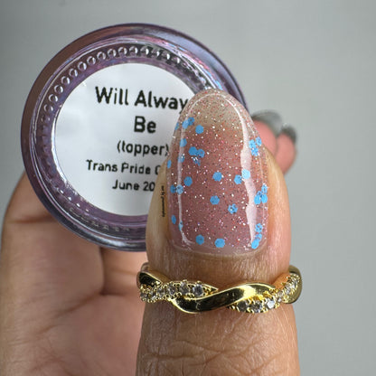 Finger with glittery nail polish holding a container labeled 'Will Always Be' on a neutral background