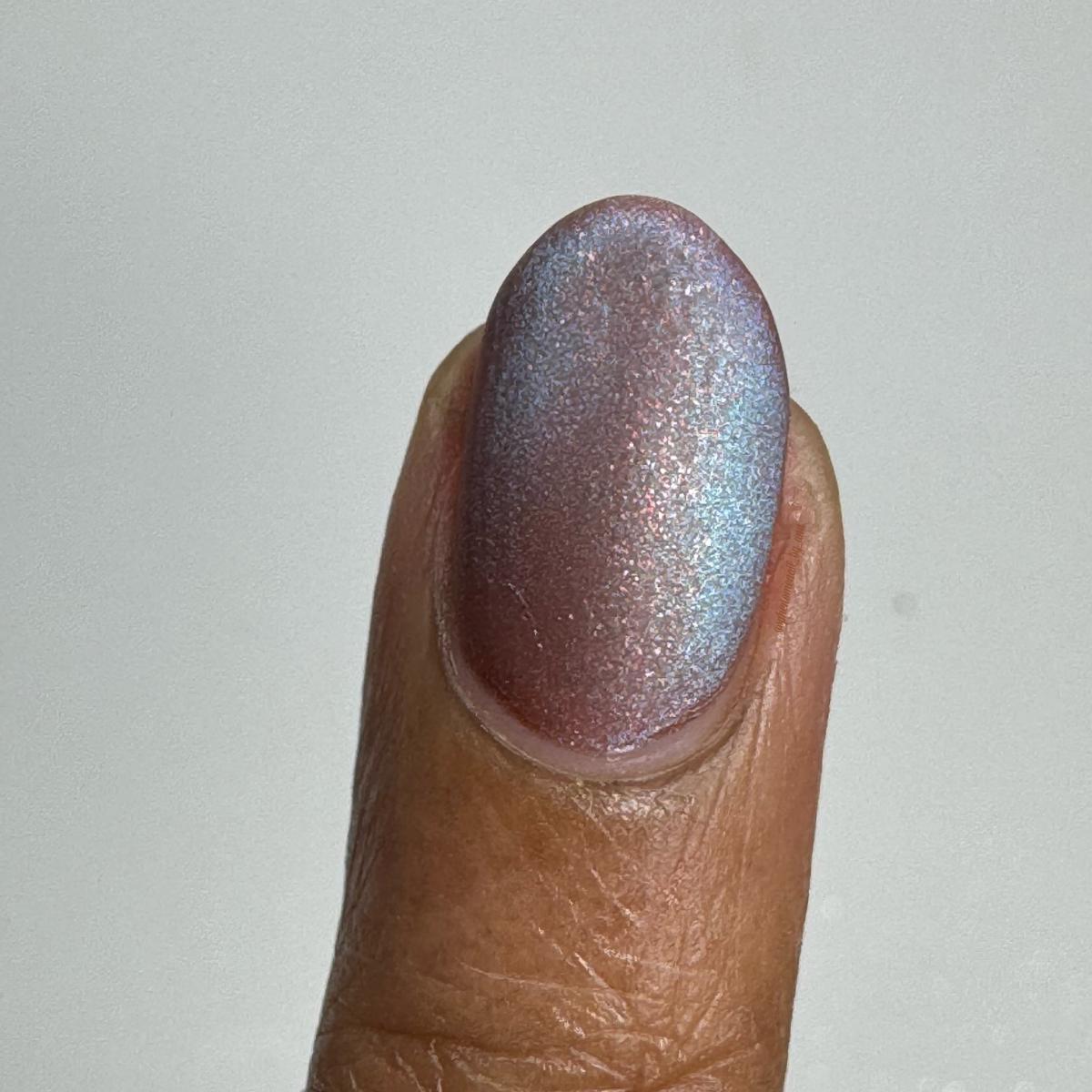 A close-up of a fingernail painted with a shimmery orange-brown nail polish that has a magnetic blue shift, topped with a matte top coat.