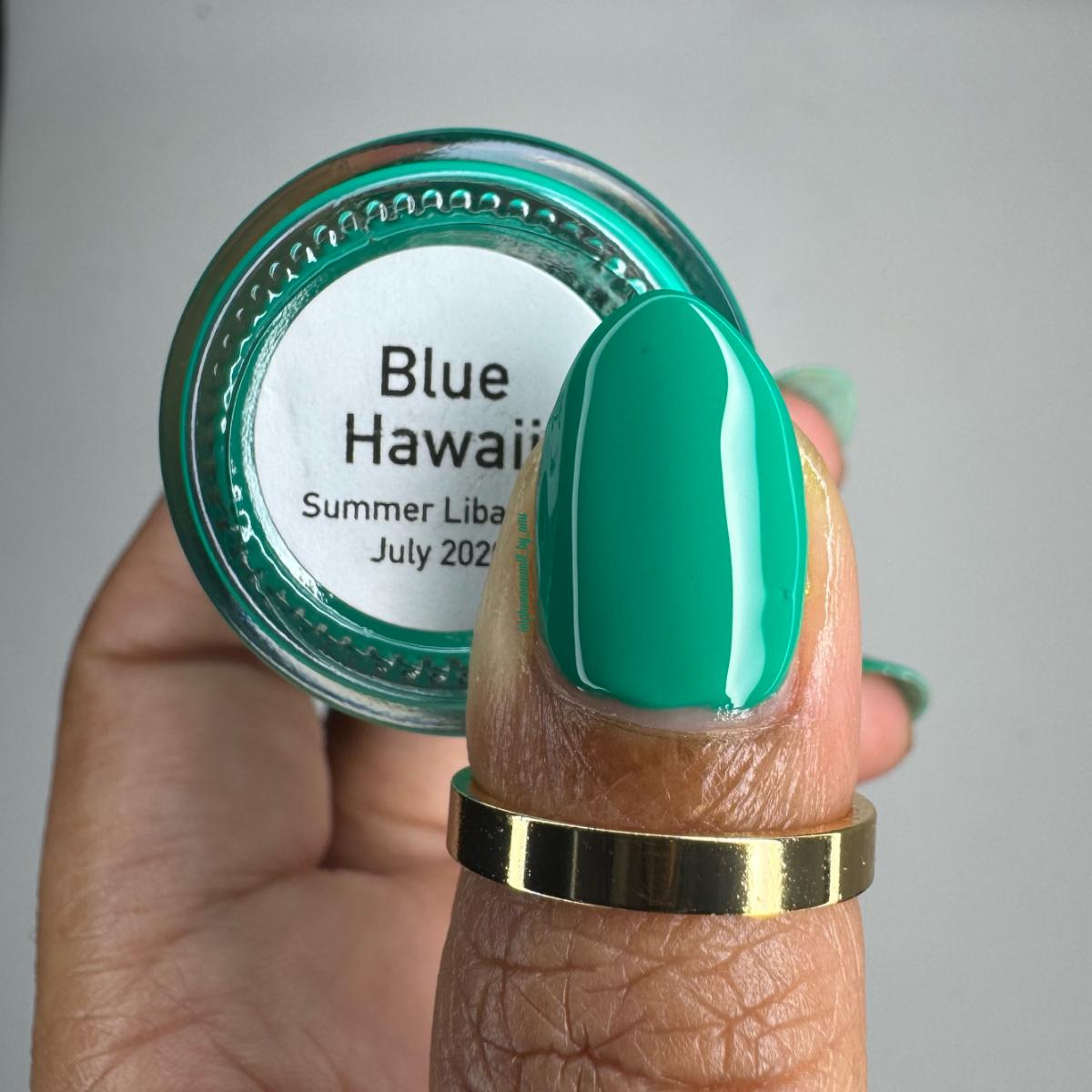 A close-up of a hand holding a small round jar labeled 'Blue Hawaii Summer Liba July 2022' while wearing a glossy mint green nail polish swatch on one finger. The product appears to be nail color or a nail polish shade.
