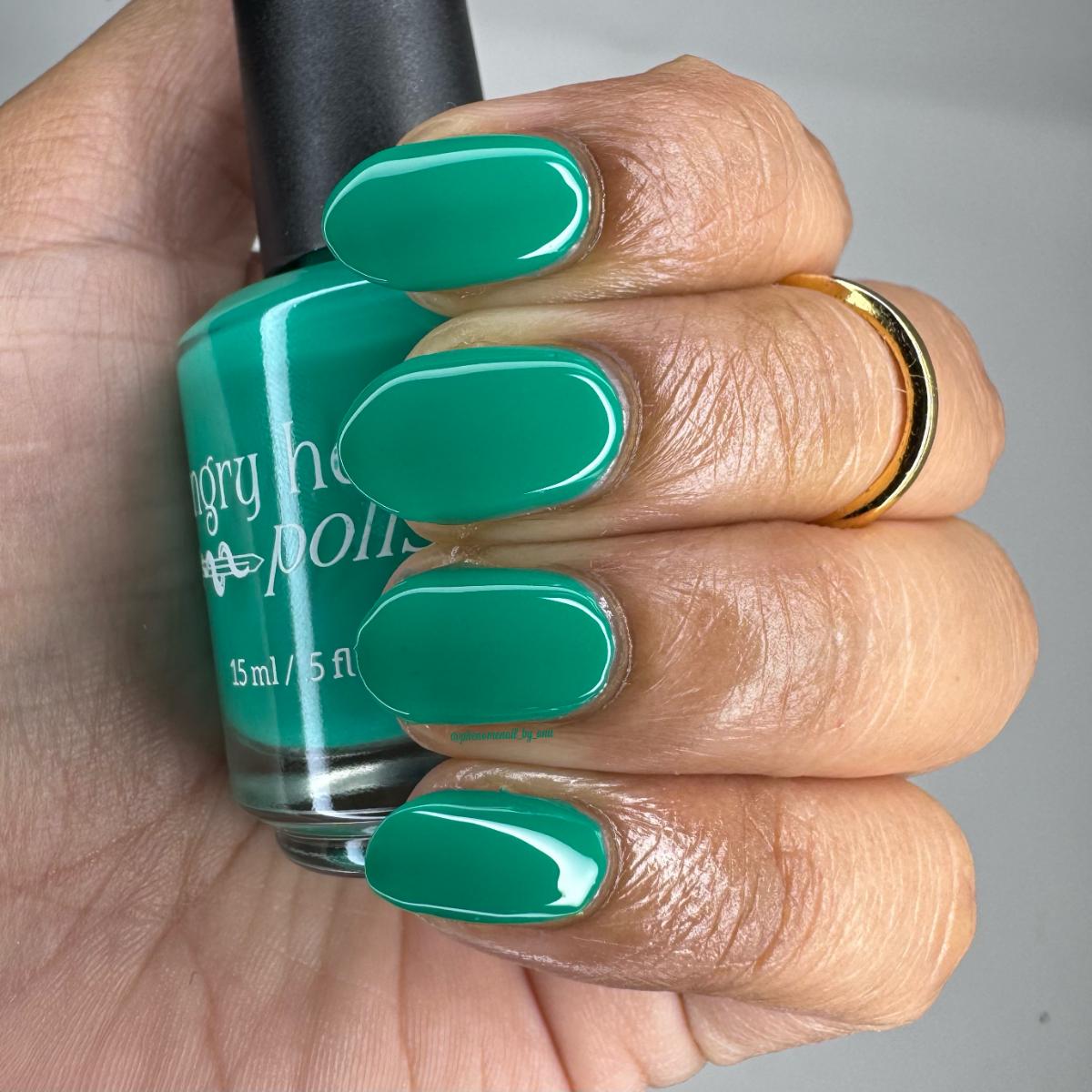 A hand with fingernails painted in a glossy bright teal-green shade holds a bottle of Angry Nail Polish. The bottle label shows the brand name 'Angry Nail Polish' and the shade name appears to be 'Green Tea'.