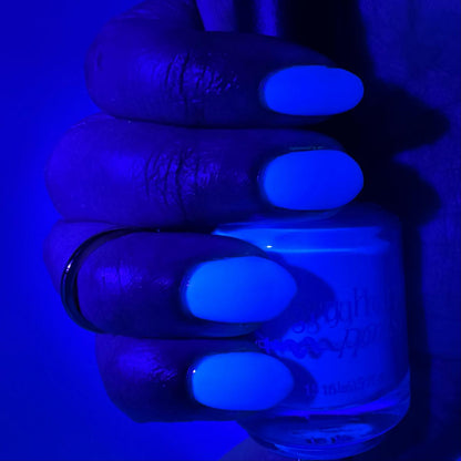 A close-up of a hand holding a nail polish bottle under blue light, showing bright neon blue painted nails and the bottle label partially visible.